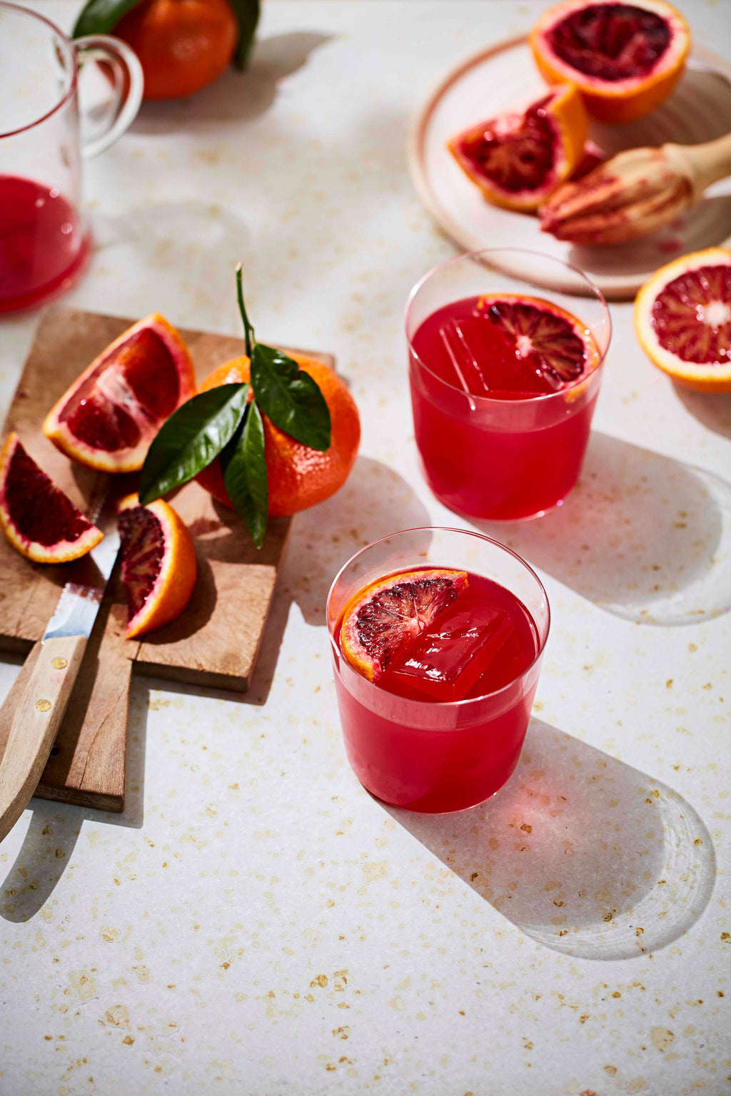 Two Gold Rush cocktails with blood orange slices on a pale worktop