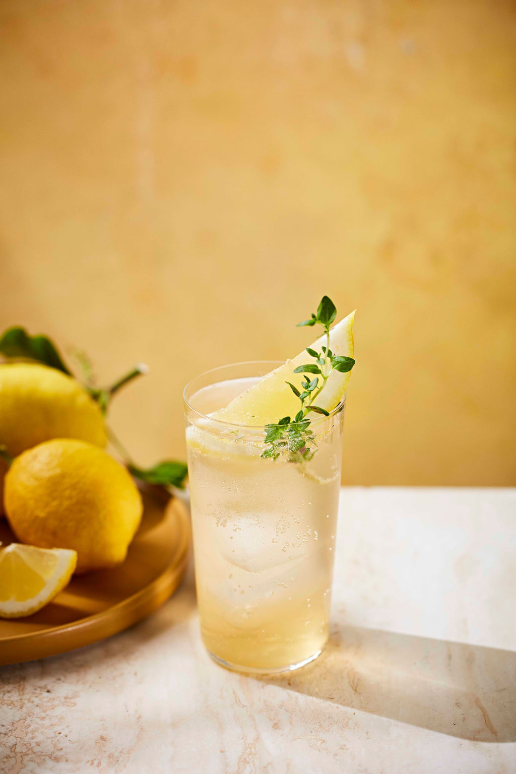 A highball of Botivo and elderflower tonic with lemon and thyme, lemons alongside
