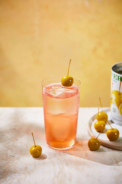 Pink Botivo and apple soda in a stubby glass with mini apples on a marble surface