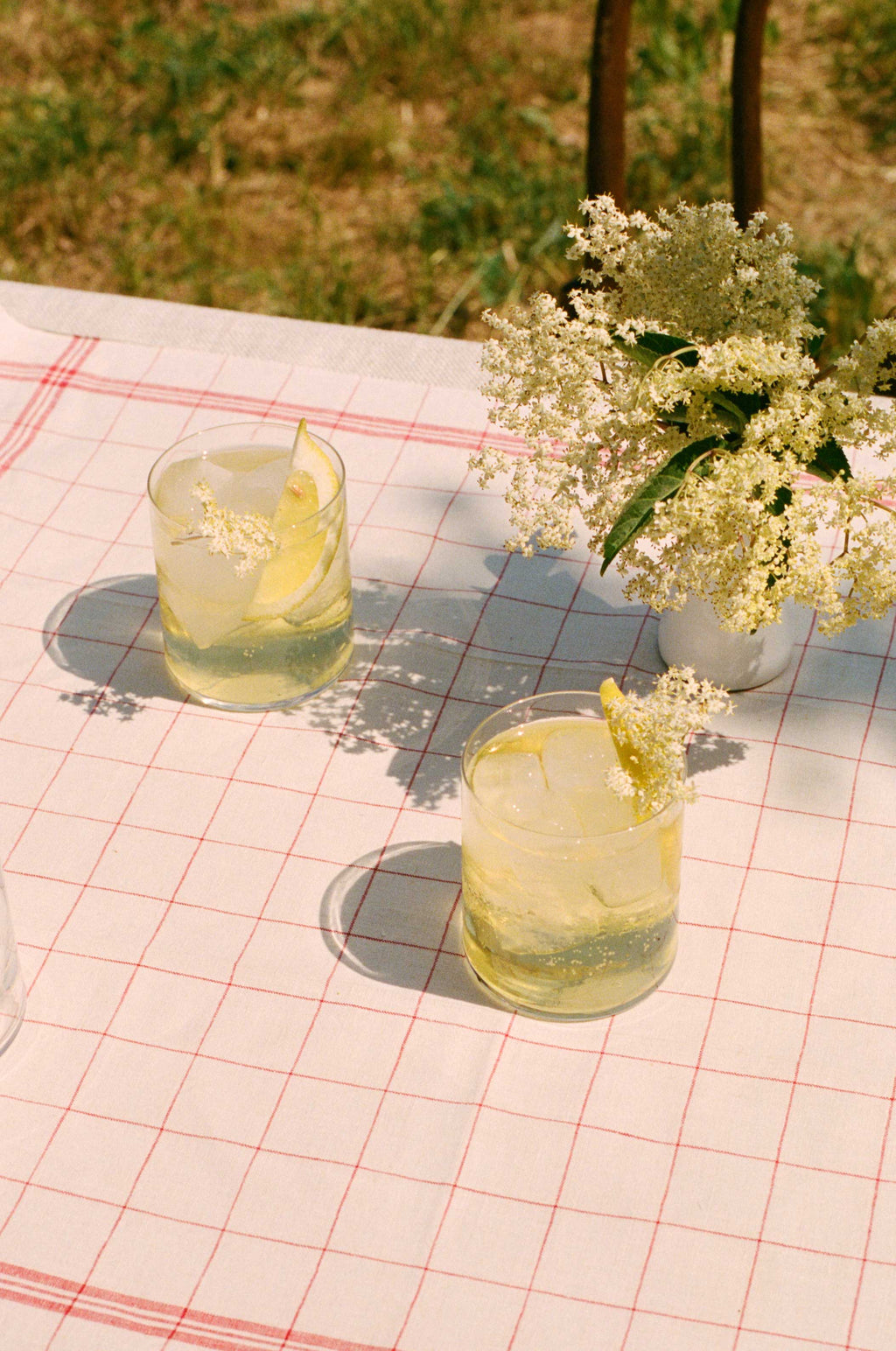 Two Elderflower Spritzes beside a jug of elderflower blossom