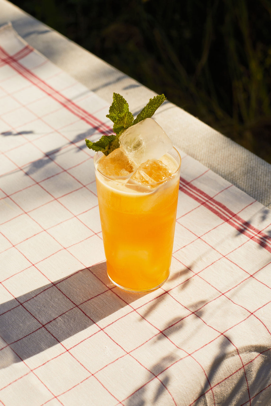 A highball of Eastern Promise with a mint sprig on a checked cloth in sunlight