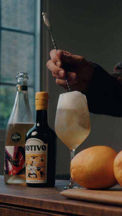 A REAL Botivo Spritz being stirred in a wine glass beside the bottles
