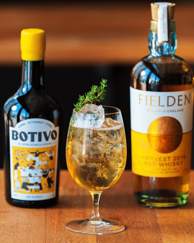 A Herbal Ley in a stemmed glass between bottles of Botivo and Fielden rye whisky