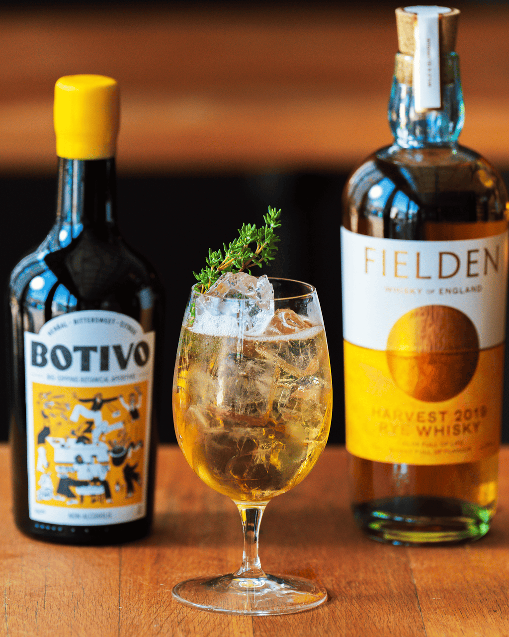 A Herbal Ley in a stemmed glass between bottles of Botivo and Fielden rye whisky