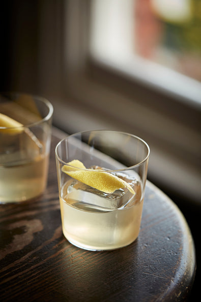 Two White Negronis in lowball glasses with lemon twists, by a window