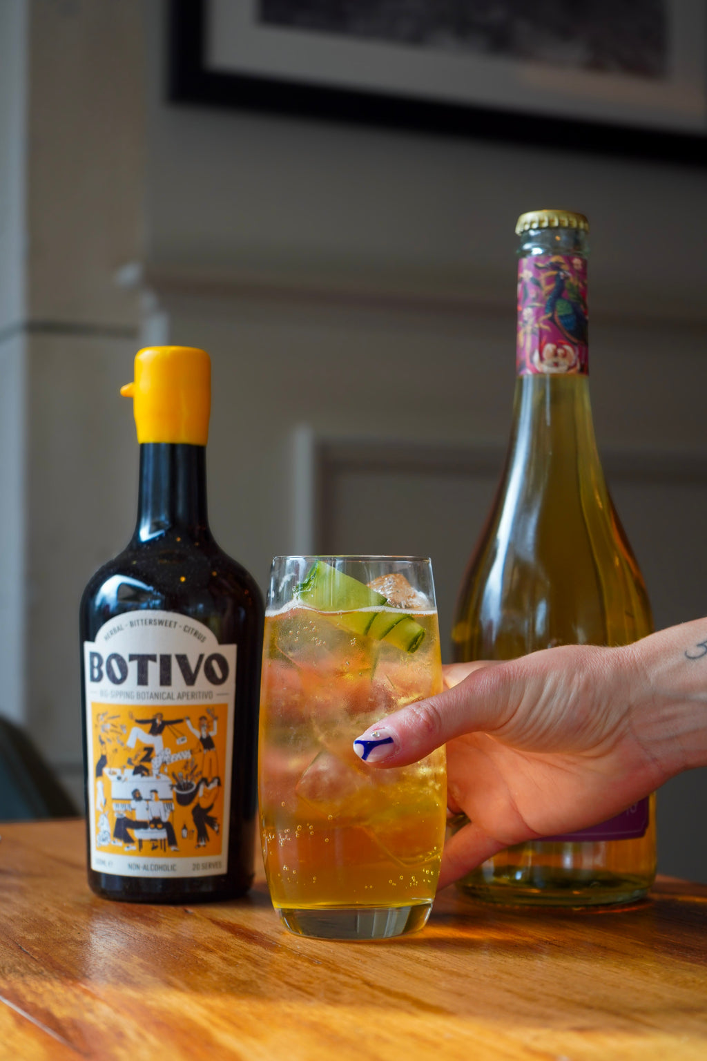 A hand holding a highball of Botivo and Saicho sparkling darjeeling beside both bottles
