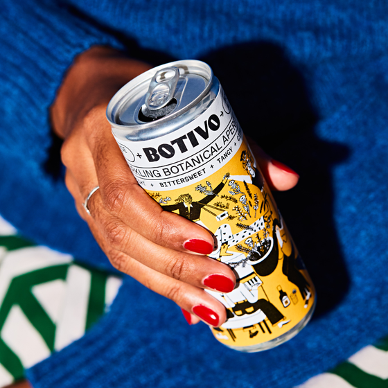 Hand with red nails holding a can of Botivo and soda against a blue jumper