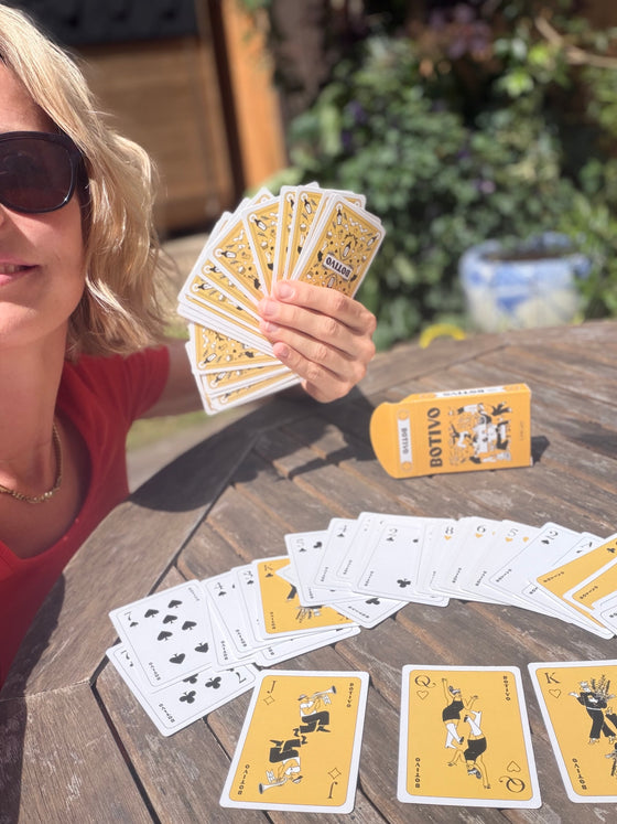 Woman holding a hand of Botivo playing cards at an outdoor table