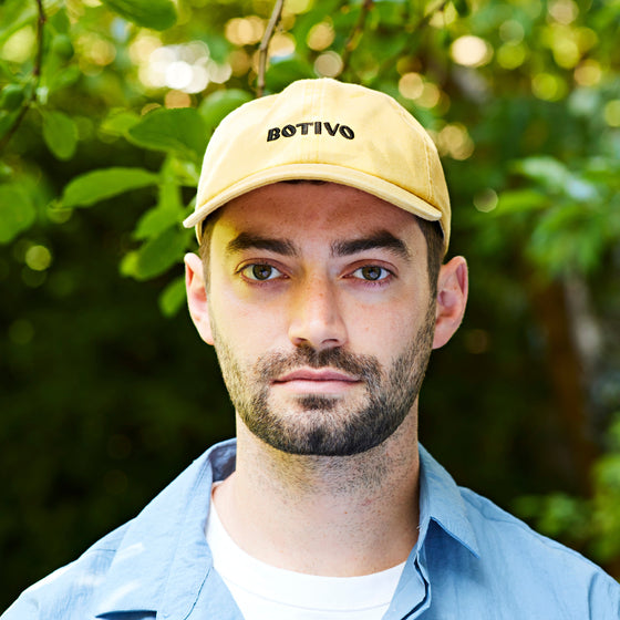 Man wearing a yellow Botivo cap outdoors in front of green leaves