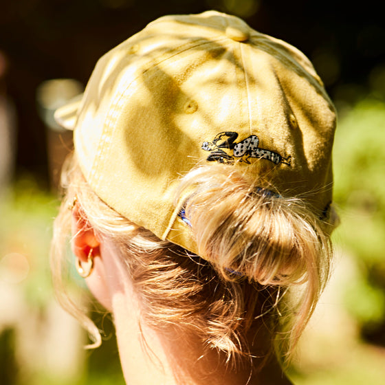 Woman wearing a yellow Botivo cap backwards, showing the embroidered character on the back