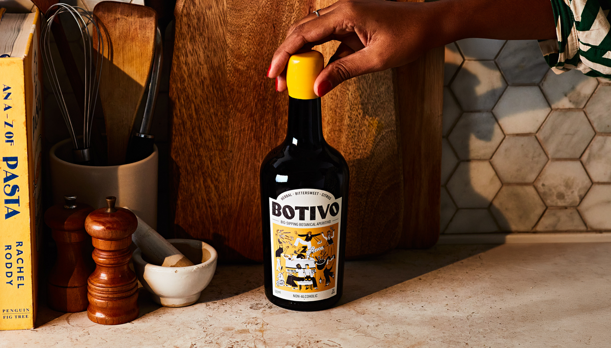 Hand placing a Botivo bottle on a kitchen worktop beside cookbooks and a pestle and mortar