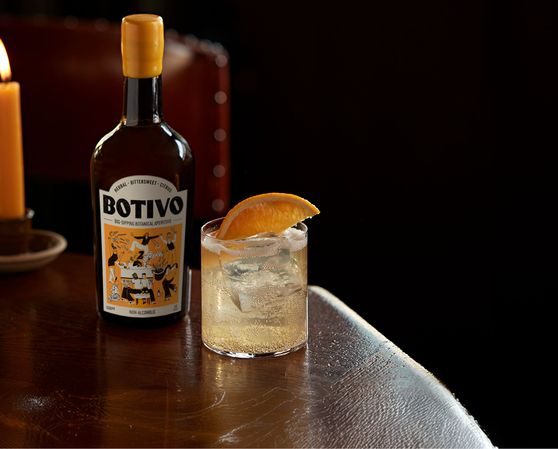 Botivo bottle and glass of Botivo with orange on a candlelit table