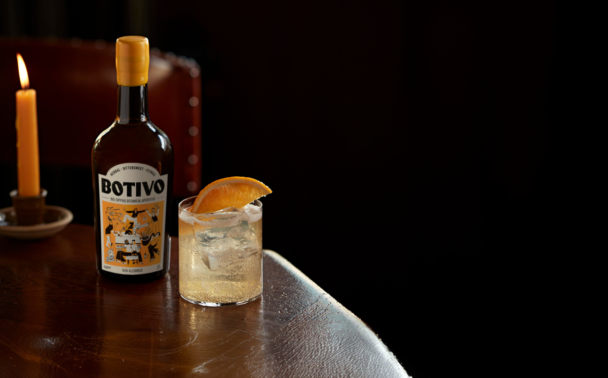 Botivo bottle and glass of Botivo with orange on a candlelit table