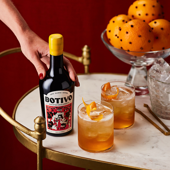 Hand placing a Botivo Wintery Botanical bottle on a drinks trolley beside glasses of Botivo and clove oranges